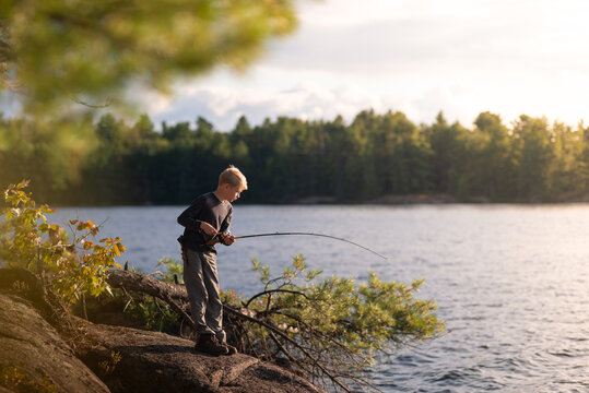 Boy on fishing trip vacation alongside lake gets bite on line