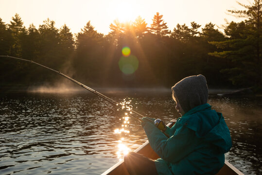 Sunrise glistens on lake water as boy fishes in canoe gets a bit