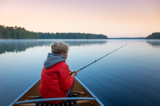 Boy fishing from canoe on serene lake early morning in Muskoka