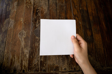 Woman hand holding white paper with wooden table background.