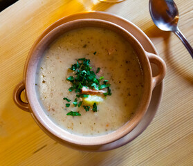 Close up of polish dish, zurek cream soup served with greens in bowl on table
