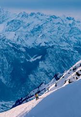 Skier in yellow jacket hiking a steep mountain snow slope carryi