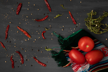 Jitomates sobre un mantel con chiles secos y pimienta sobre un fondo de color gris