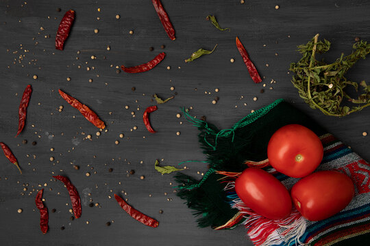 Jitomates sobre un mantel con chiles secos y pimienta sobre un fondo de color gris