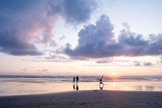 Siblings play on sandy beach at sunset