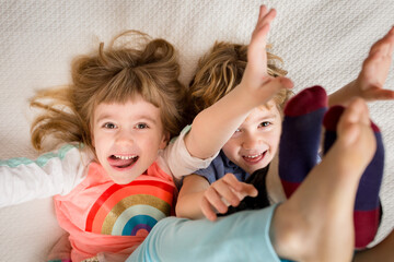 Children laying on a bed laugh and reach for viewer