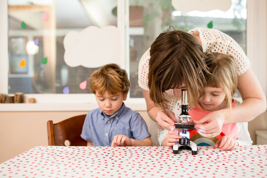 Mother and children set up a microscope at dining table