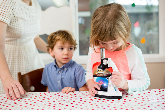 Smiling girl looks into microscope while brother watches