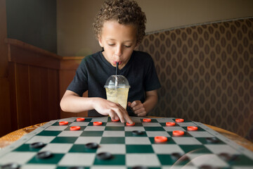 Boy playing checkers while sipping from cup
