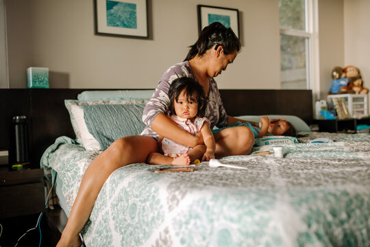 Asian-American deaf mother with cochlear implant sitting on bed caring for sick children 