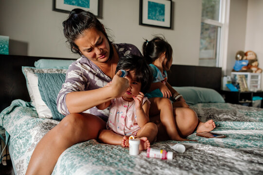 Asian-American mom on bed with sick girls