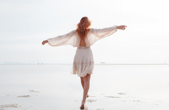 Graceful woman in white clothing walking on seashore