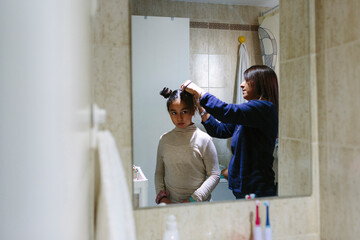 10-year old hispanic girl getting her hair done by her mother