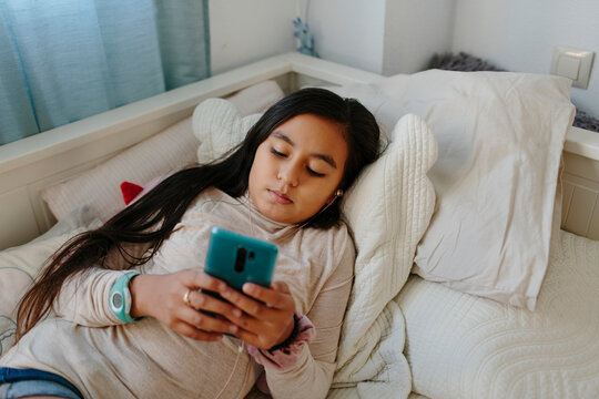 Hispanic 10 year old girl using a cell phone on the bed 