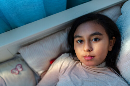 Hispanic 10-year old girl laying on bed looking at camera.