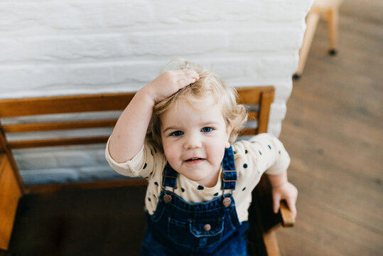 sweet little girl with curls sittting on a vintage wooden bench while touching her head