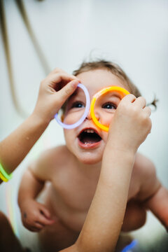 Little baby girl playing with glow sticks in a bath with water