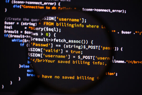 Software code on a monitor screen with a magnifying glass - Powered by Adobe