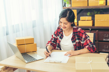 Woman checking stock goods supply delivery package shipping use document checklist. Asian woman startup small business at home office. Online entrepreneur asian woman use tablet checking online order