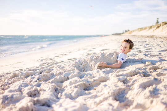 Smiling boy enjoying playing in sand at the beach on a sunny aft