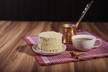 A buttercream cake, a cup of coffee, cinnamon sticks and a turk on the table.