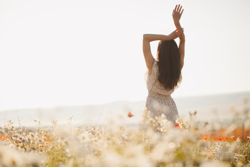 Beautiful girl in summer dress walks in a flower field