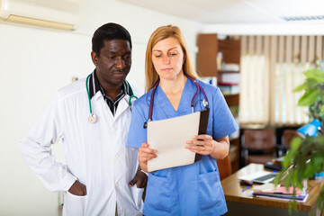 Experienced african american doctor advising his young female colleague about diagnosis of patient...