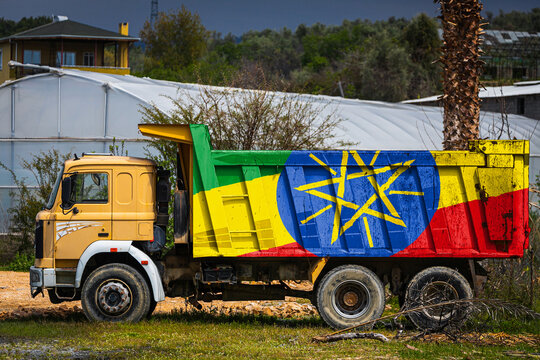 Dump truck with the image of the national flag of Ethiopia is parked against the background of the countryside. The concept of export-import, transportation, national delivery of goods