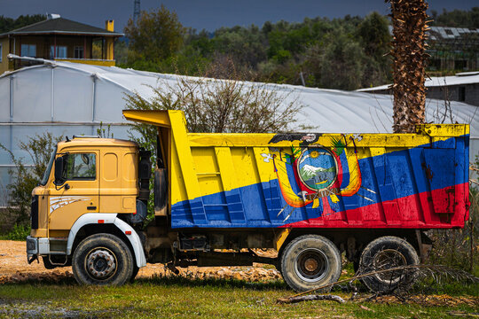 Dump truck with the image of the national flag of Ecuador is parked against the background of the countryside. The concept of export-import, transportation, national delivery of goods