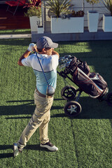 Hombre practicando swing de golf, con su carro y palos - obrazy, fototapety, plakaty