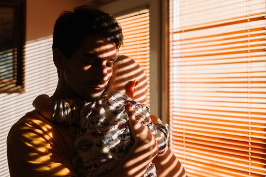 Father lullaby his baby by the window light.