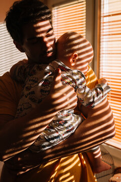 Father holds baby and lullaby by the darken window 