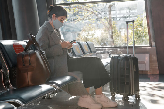 Female passenger in mask using smartphone in airport