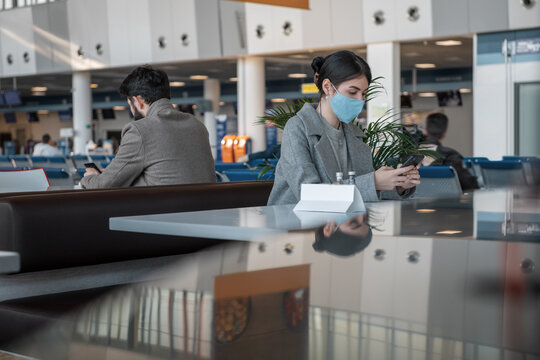 Female traveler in mask using smartphone near man in cafe