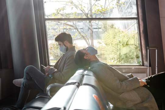 Woman in mask resting near man with smartphone in airport waiting room
