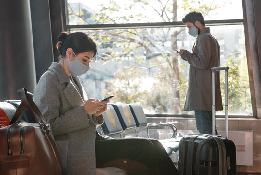 Travelers in masks browsing smartphones in airport waiting room