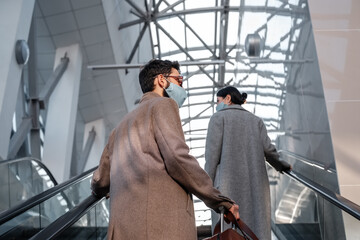 Man in mask riding escalator near woman