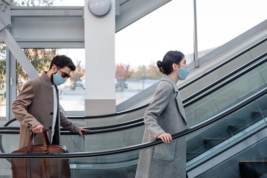 Travelers in masks riding moving stairs - Powered by Adobe