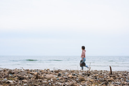 Woman with plastic bag walking on dirty seashore