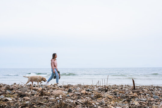Woman with dog walking on polluted seashore