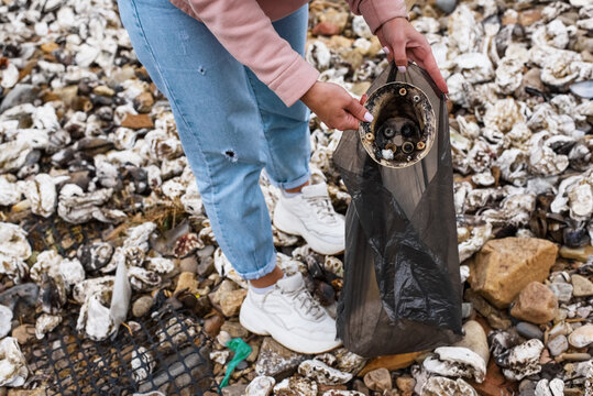 Crop woman showing discarded cup on seashore