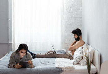Man and woman with gadgets resting on bed