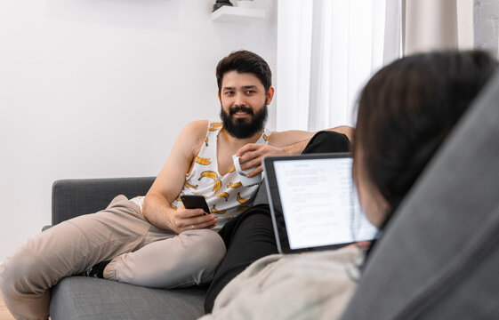 Man with smartphone and hot drink resting near woman with tablet