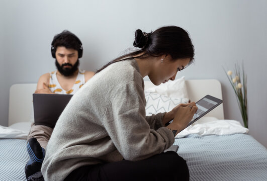 Woman using tablet near man with laptop on bed
