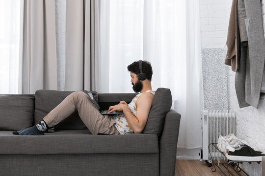 Male hipster in headphones using laptop on sofa