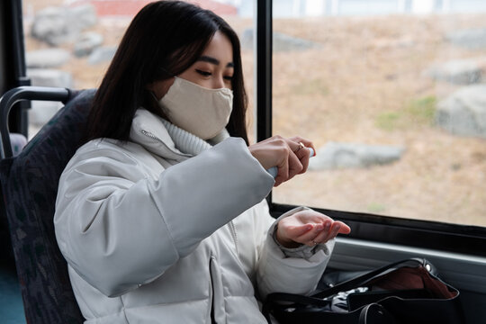 Ethnic female disinfecting hands during bus ride