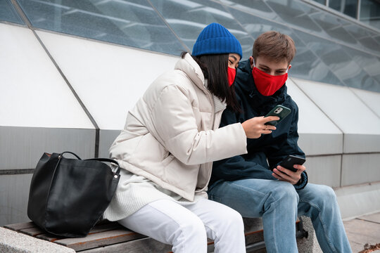 Ethnic female in mask sharing data on smartphone with boyfriend