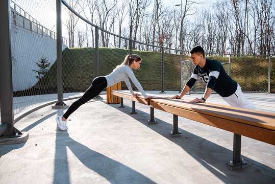Young man and woman exercising on bench on sports ground