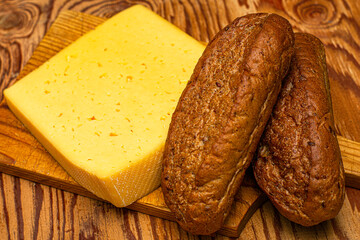 a piece of cheese and two rye bread rolls on a cutting board on a wooden table Rustic collection. Organic food. Organic product.