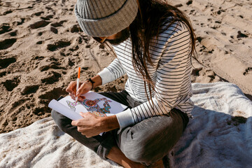 man sitting on beach sand drawing mandala